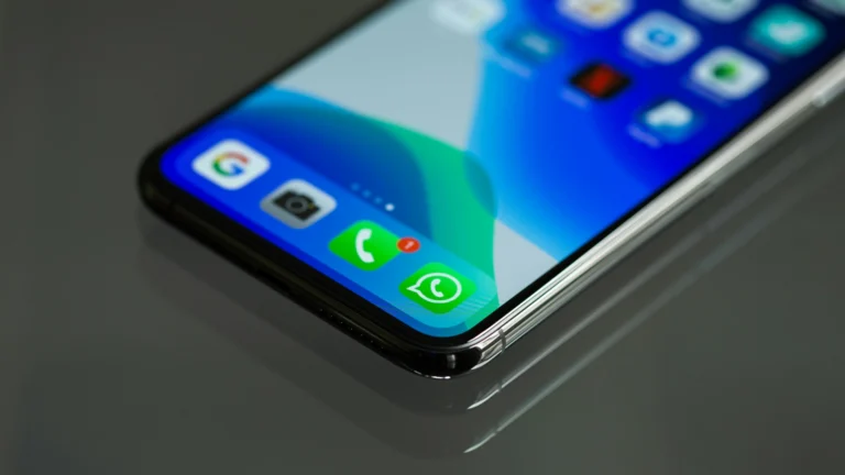 Tampilan close-up smartphone dengan ikon aplikasi WhatsApp hijau di dock layar yang elegan.