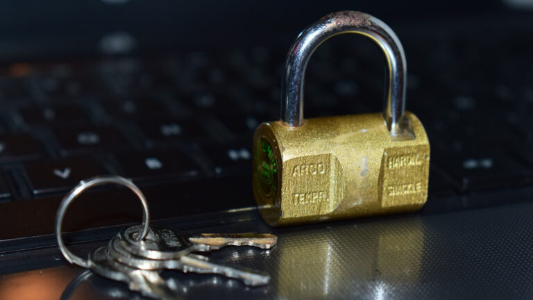 Gembok kuningan dan gantungan kunci di atas keyboard laptop sebagai ilustrasi keamanan sistem dan izin akses (permissions) pada Linux.